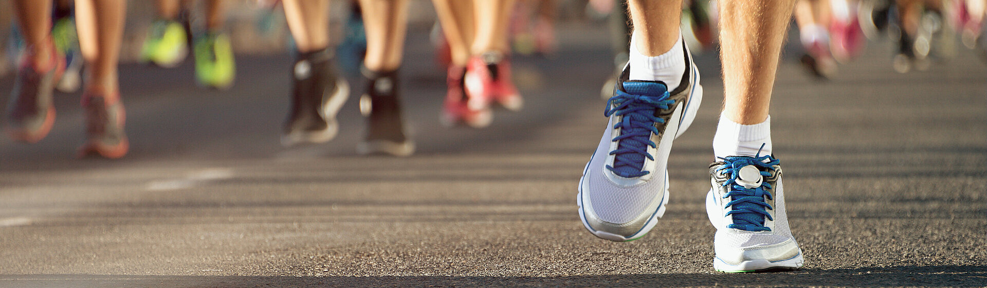 Nahaufnahme der Sportschuhe mehrerer Läufer während eines Marathons, die sich auf der Strecke fortbewegen.